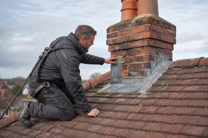 A roofer inspecting chimney flashing for early signs of roof damage